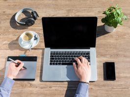 picture of a person working on a laptop on a desk with a coffe cup, headphones and smartphone