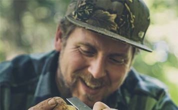 A man joyfully using a pocket knife in Australia to peel a mushroom during a nature hike, demonstrating the practicality of having a pocket knife while exploring the Australian wilderness.